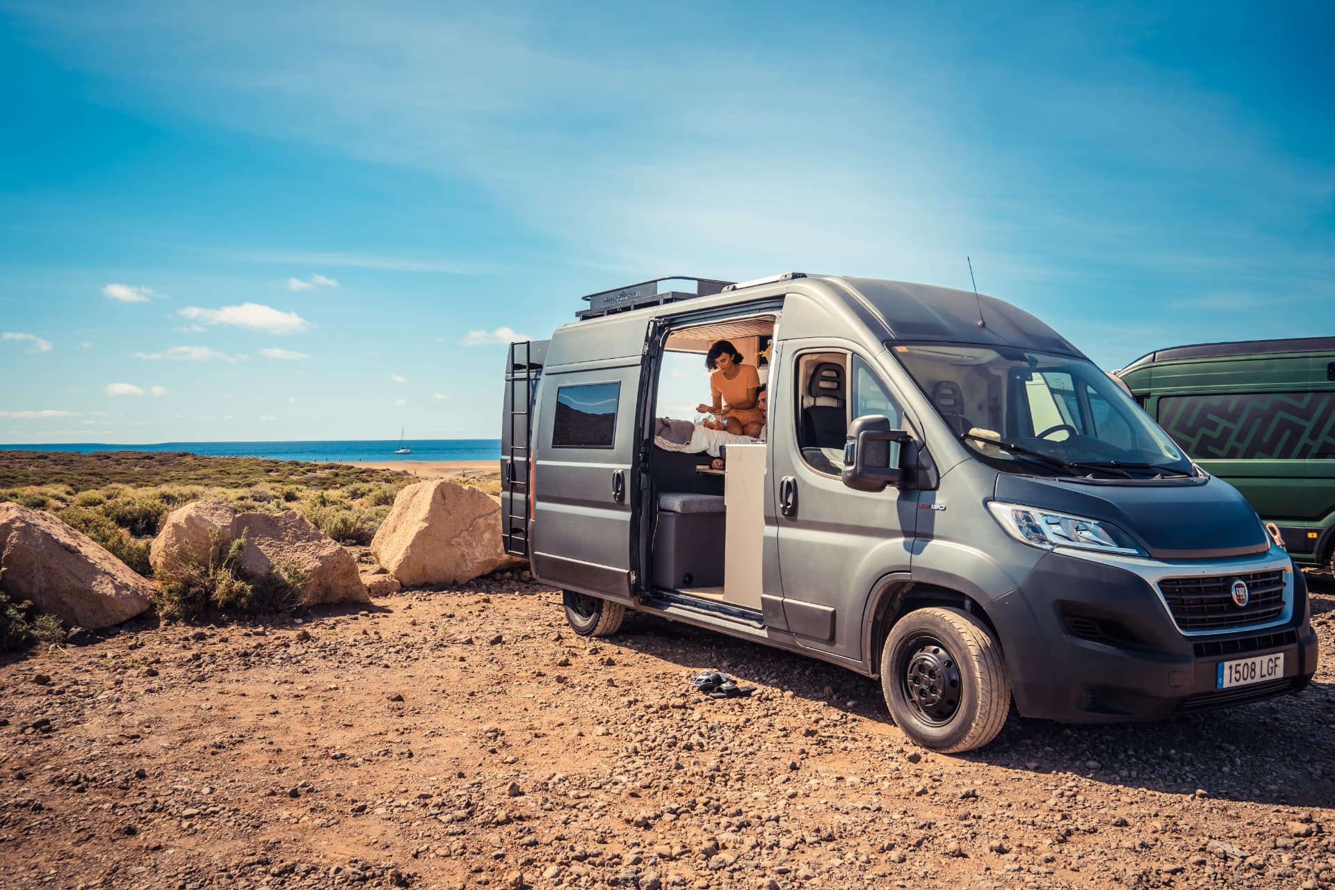 Fiat Ducato camper gris con la puerta lateral abierta frente a una playa de Tenerife