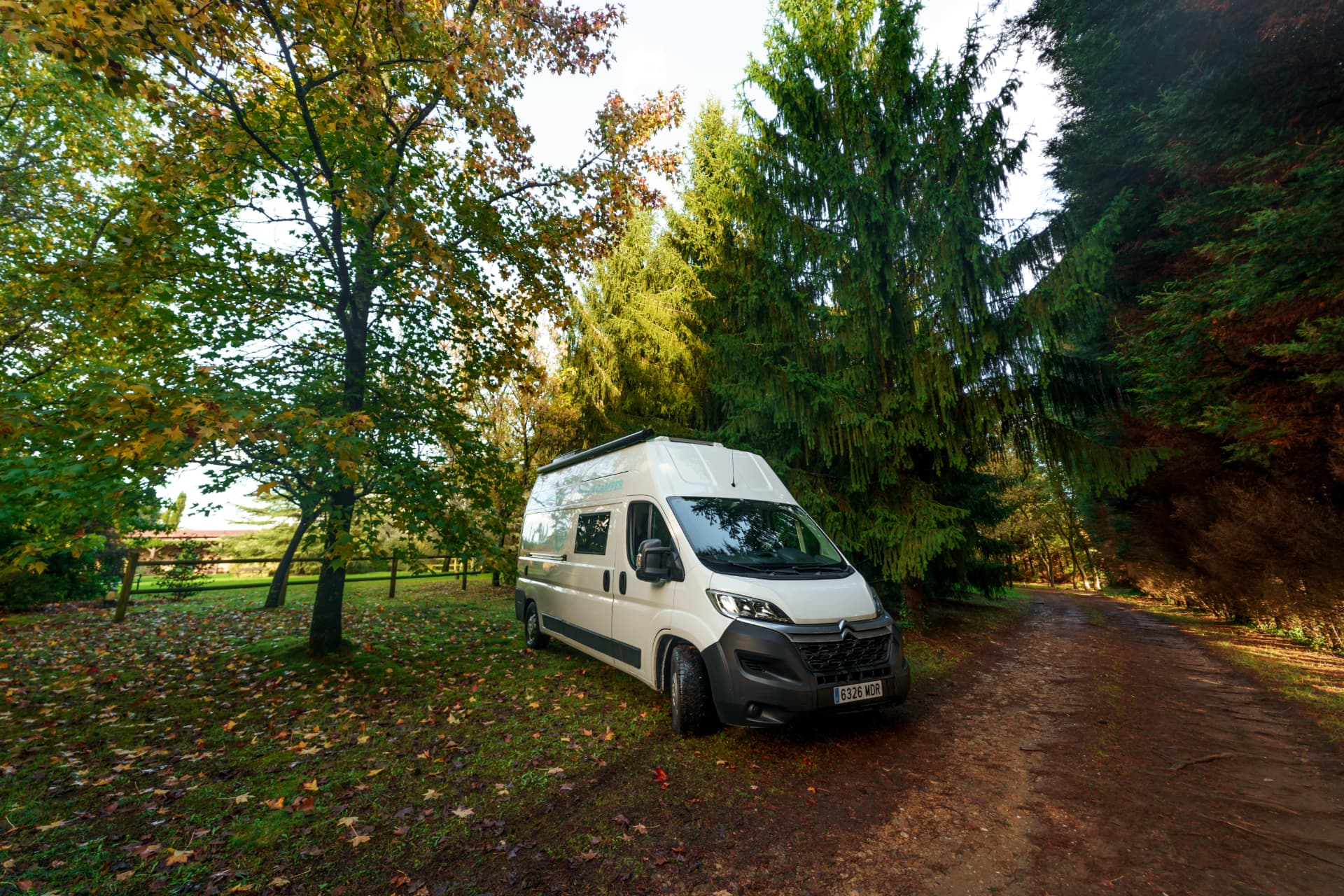 Citroën Jumper camper blanca aparcada entre árboles en otoño