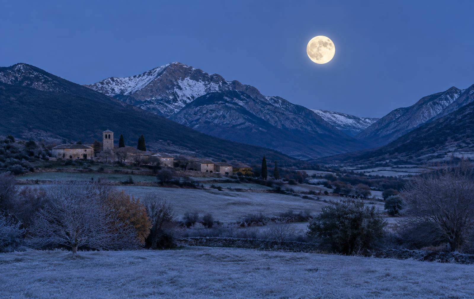 Luna llena sobre un valle de montaña con escarcha al anochecer